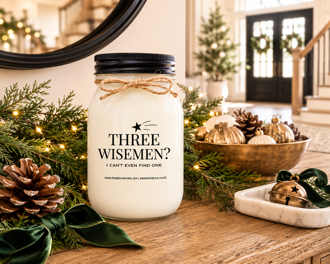 THREE WISE MEN? I CAN'T EVEN FIND ONE Christmas candle displayed on a reclaimed white oak farmhouse entry console with cedar garland, forest green velvet ribbon, pinecones, antique brass accents, and a bright luxury foyer decorated for the holidays.