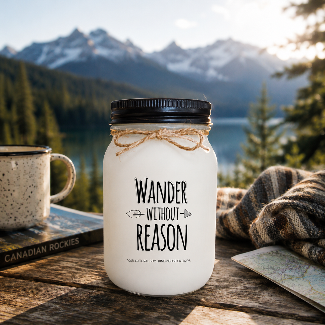 WANDER WITHOUT REASON soy candle with black lid displayed on a rustic wooden dock overlooking a mountain lake at sunrise, surrounded by pine trees and breathtaking mountain views.