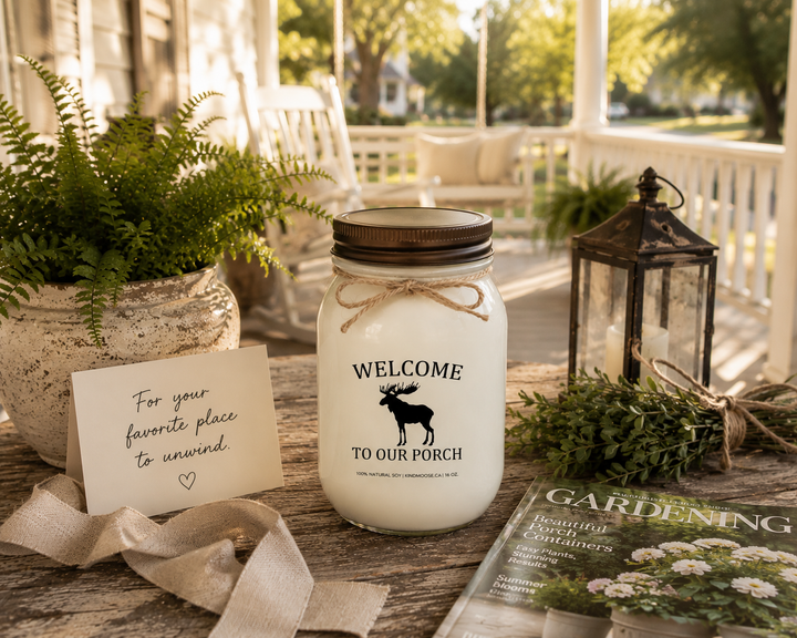 WELCOME TO OUR PORCH soy candle with distressed bronze lid styled as a thoughtful porch-themed gift featuring a handwritten card, gardening magazine, lantern, greenery, linen ribbon, and farmhouse porch décor.