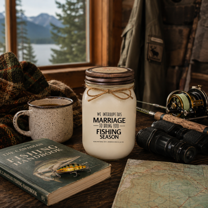 WE INTERRUPT THIS MARRIAGE TO BRING YOU FISHING SEASON soy candle with distressed bronze lid styled beside a fishing tackle box, coffee mug, fishing magazine, plaid blanket, and dockside fishing gear at a cozy Canadian cottage.