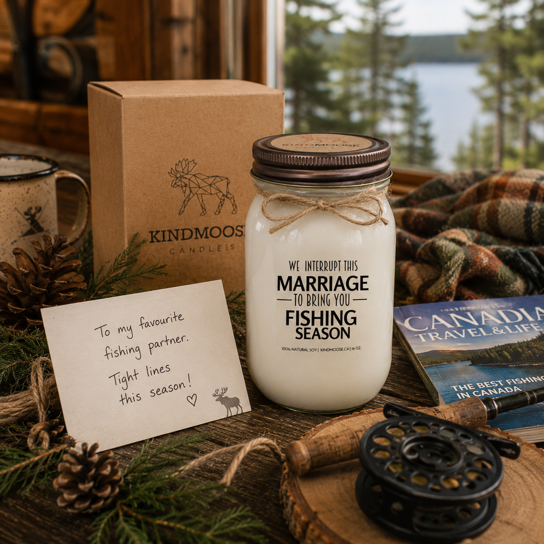 WE INTERRUPT THIS MARRIAGE TO BRING YOU FISHING SEASON soy candle with distressed bronze lid styled as a thoughtful fishing-themed gift beside a handwritten card, fishing magazine, coffee mug, pinecones, evergreen sprigs, and rustic cottage décor.