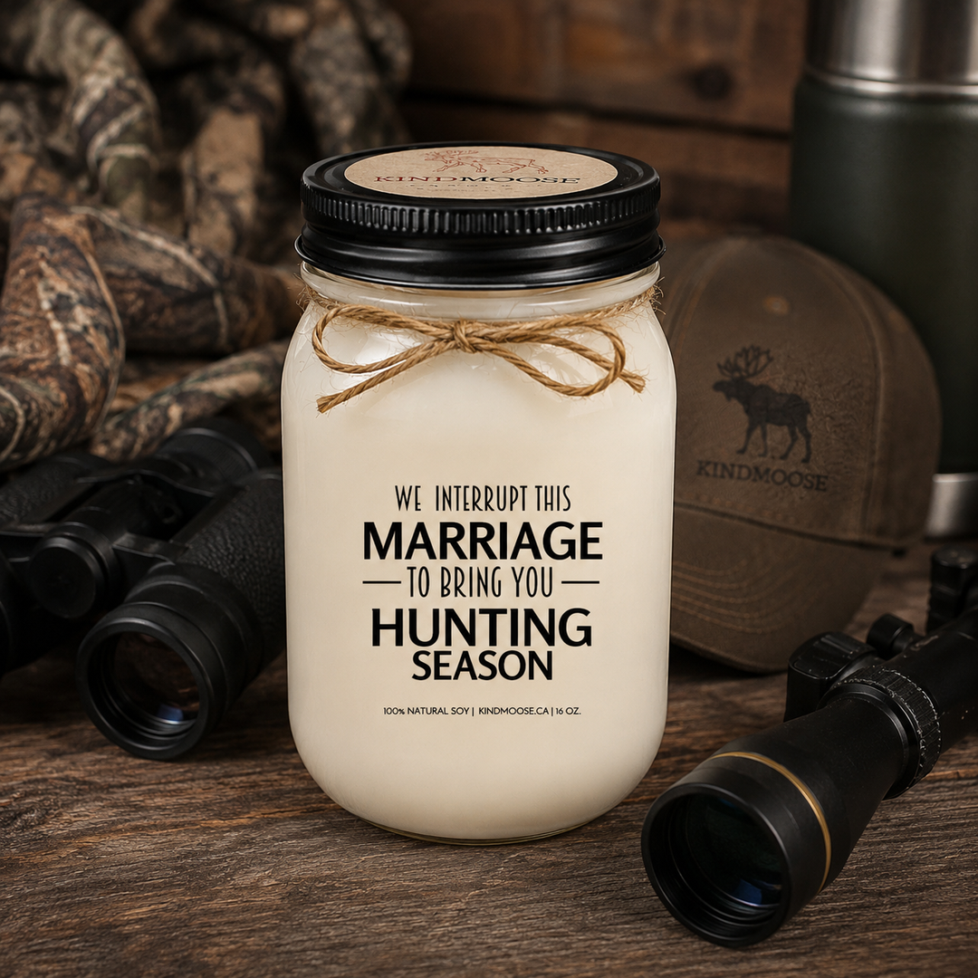 WE INTERRUPT THIS MARRIAGE TO BRING YOU HUNTING SEASON soy candle with black lid displayed on a rustic cottage dock overlooking a peaceful lake at sunrise, surrounded by pine trees, calm water, and the beauty of the Canadian outdoors.