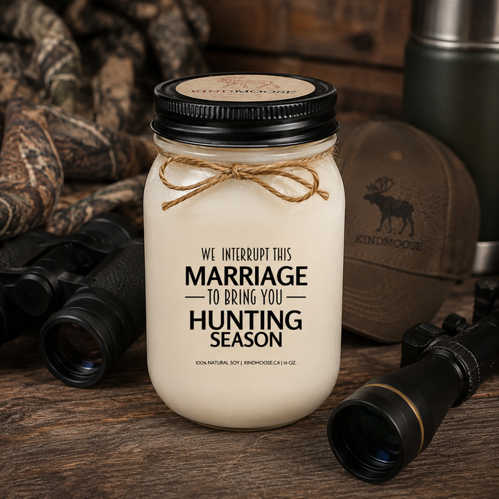 WE INTERRUPT THIS MARRIAGE TO BRING YOU HUNTING SEASON soy candle with black lid displayed on a rustic cottage dock overlooking a peaceful lake at sunrise, surrounded by pine trees, calm water, and the beauty of the Canadian outdoors.