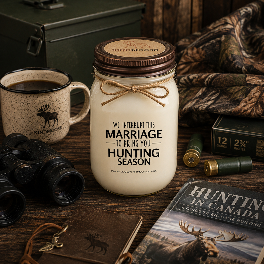WE INTERRUPT THIS MARRIAGE TO BRING YOU HUNTING SEASON soy candle with distressed bronze lid styled beside a coffee mug, hunting guidebook, binoculars, camouflage blanket, and outdoor gear inside a cozy hunting cabin.
