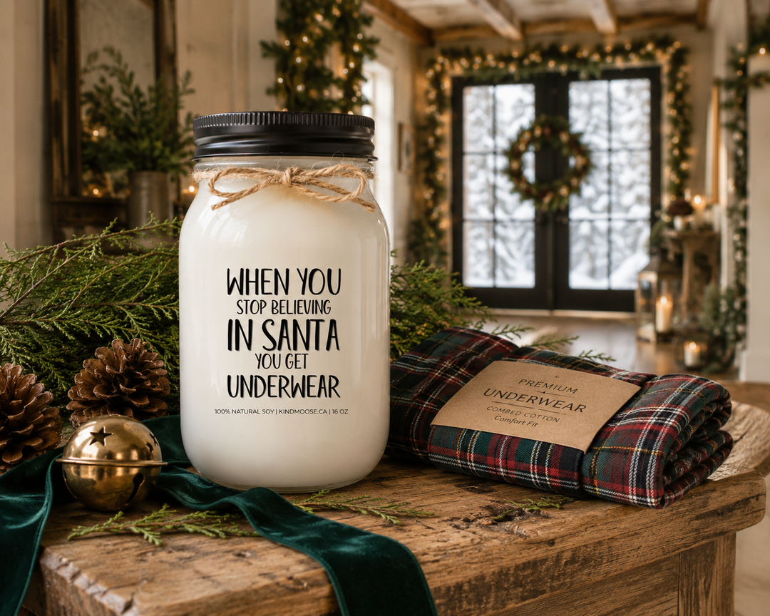 WHEN YOU STOP BELIEVING IN SANTA YOU GET UNDERWEAR customizable Christmas candle displayed on a reclaimed white oak console table with fresh cedar, pinecones, a brass sleigh bell, a gift-boxed pair of plaid underwear, and elegant holiday décor inside a luxury Canadian modern farmhouse.