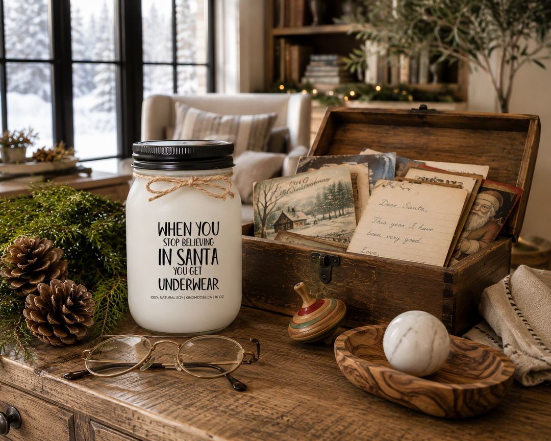 WHEN YOU STOP BELIEVING IN SANTA YOU GET UNDERWEAR customizable Christmas candle displayed beside a vintage Christmas keepsake box filled with childhood letters to Santa, old Christmas cards, reading glasses, cedar sprigs, and pinecones on a reclaimed white oak library table inside a luxury Canadian farmhouse.